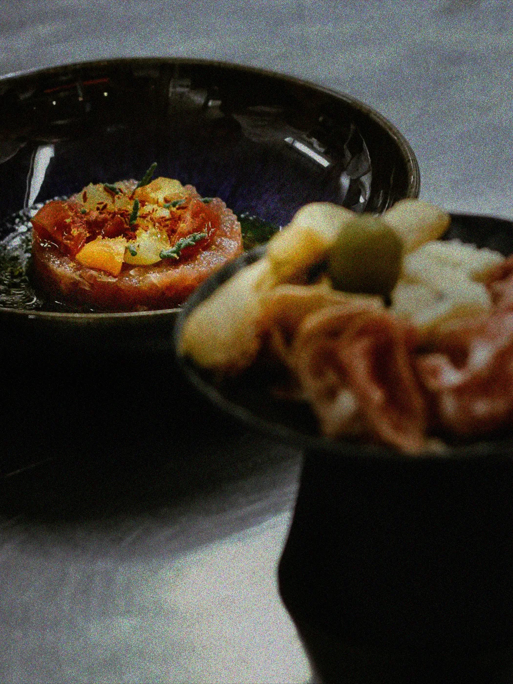 Zwei Keramikteller mit einem angerichteten Thunfisch-Tatar und einer Auswahl an Antipasti.