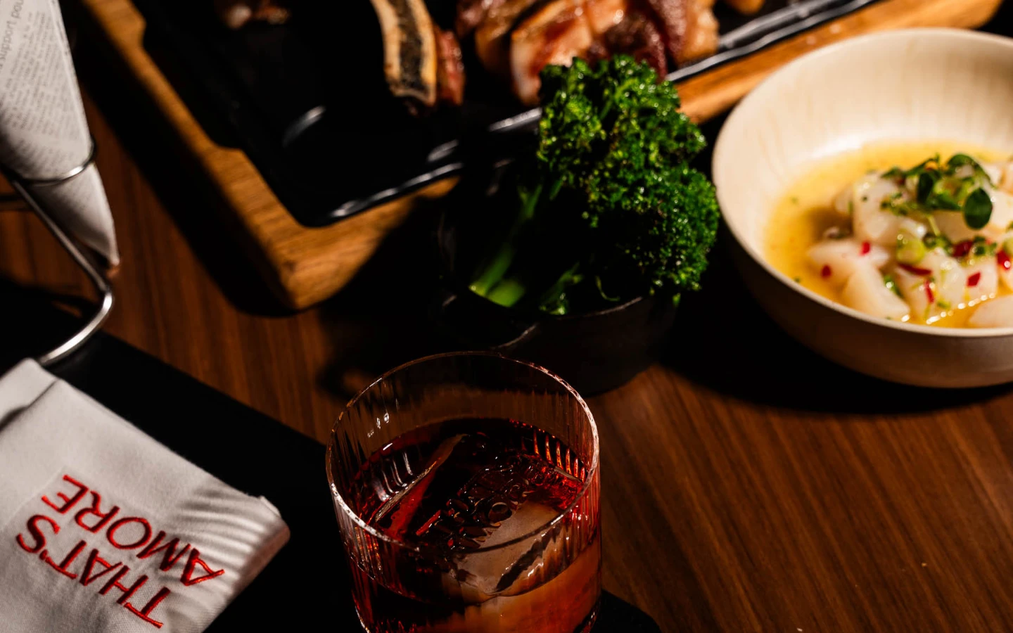 Steak auf Holzbrett, daneben Cocktail, Fisch-Carpaccio im Schälchen, Brokkoli auf Teller angerichtet.