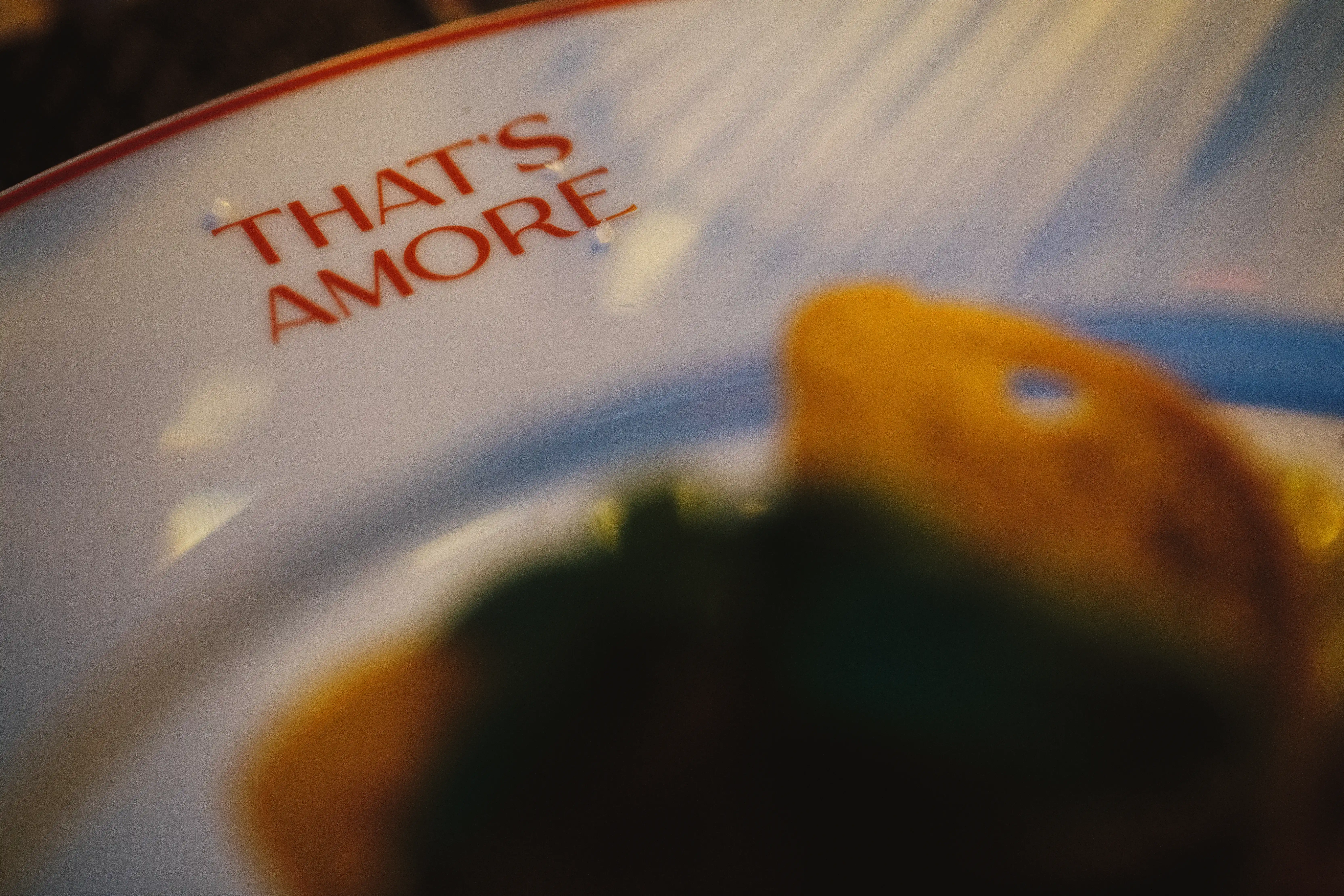 Detailaufnahme eines weißen Tellers mit rotem Schriftzug THAT’S AMORE am Rand.