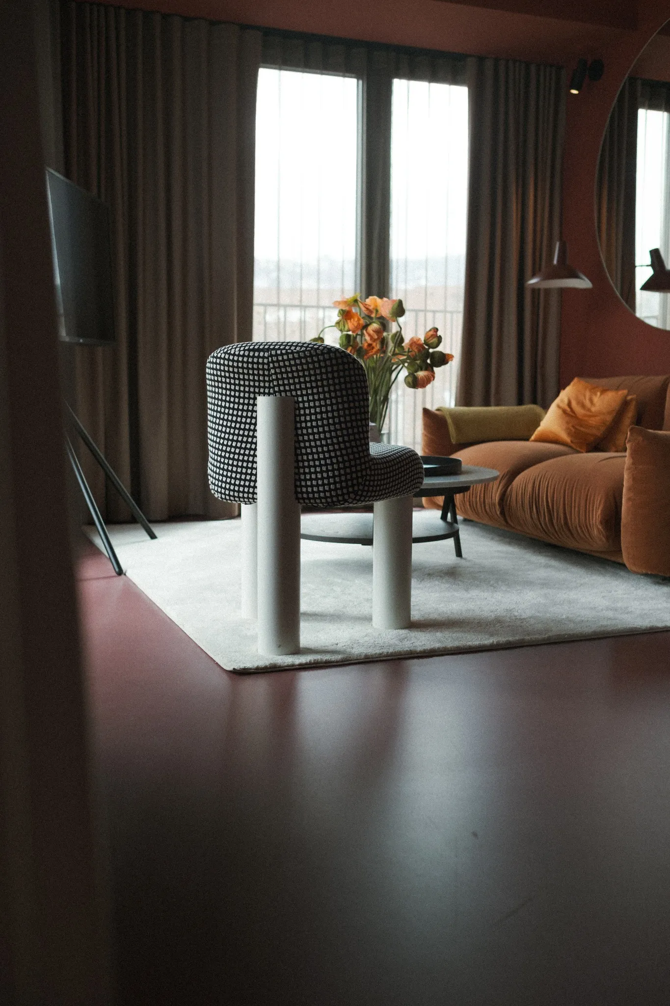 Design-Suite im EmiLu Hotel mit modernem Sessel, Blumendekoration und gemütlichem Sofa vor bodentiefen Fenstern.