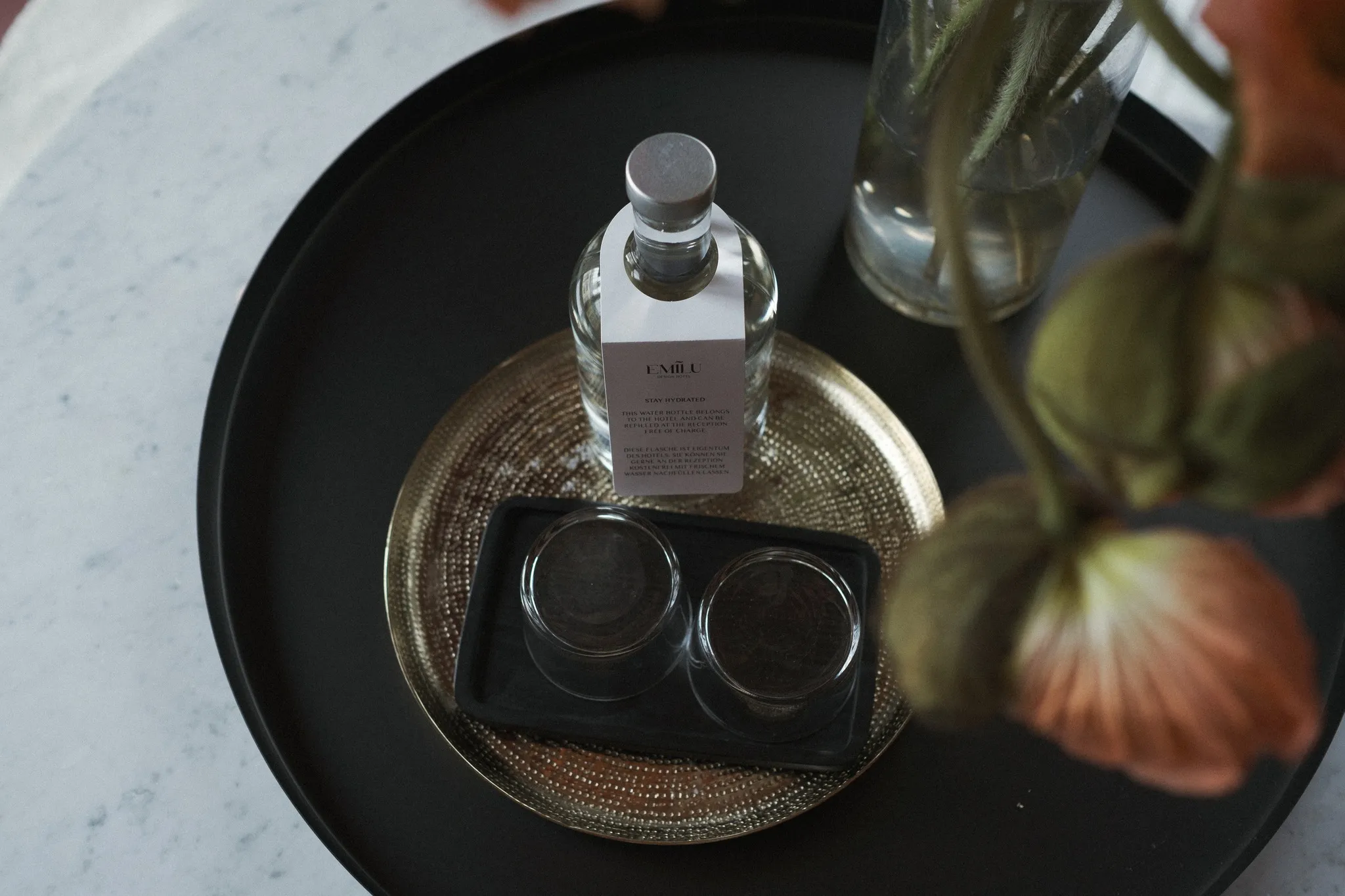 Detailaufnahme eines Tabletts mit Wasserflasche, Gläsern und frischen Blumen als Begrüßung im EmiLu Hotel.
