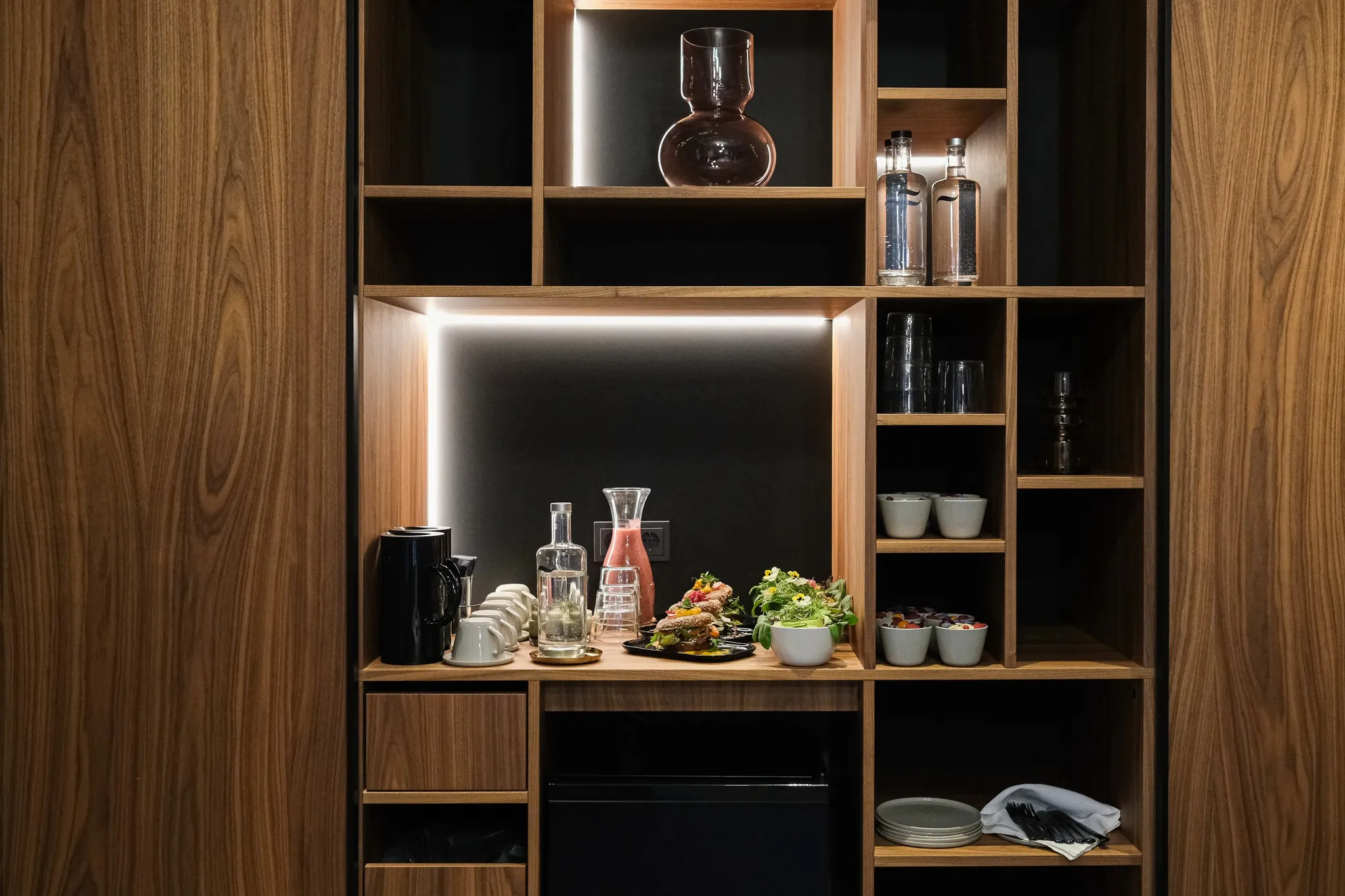 Stilvolle Minibar im EmiLu Hotel mit Holzregalen, Getränken, Snacks und Geschirr.