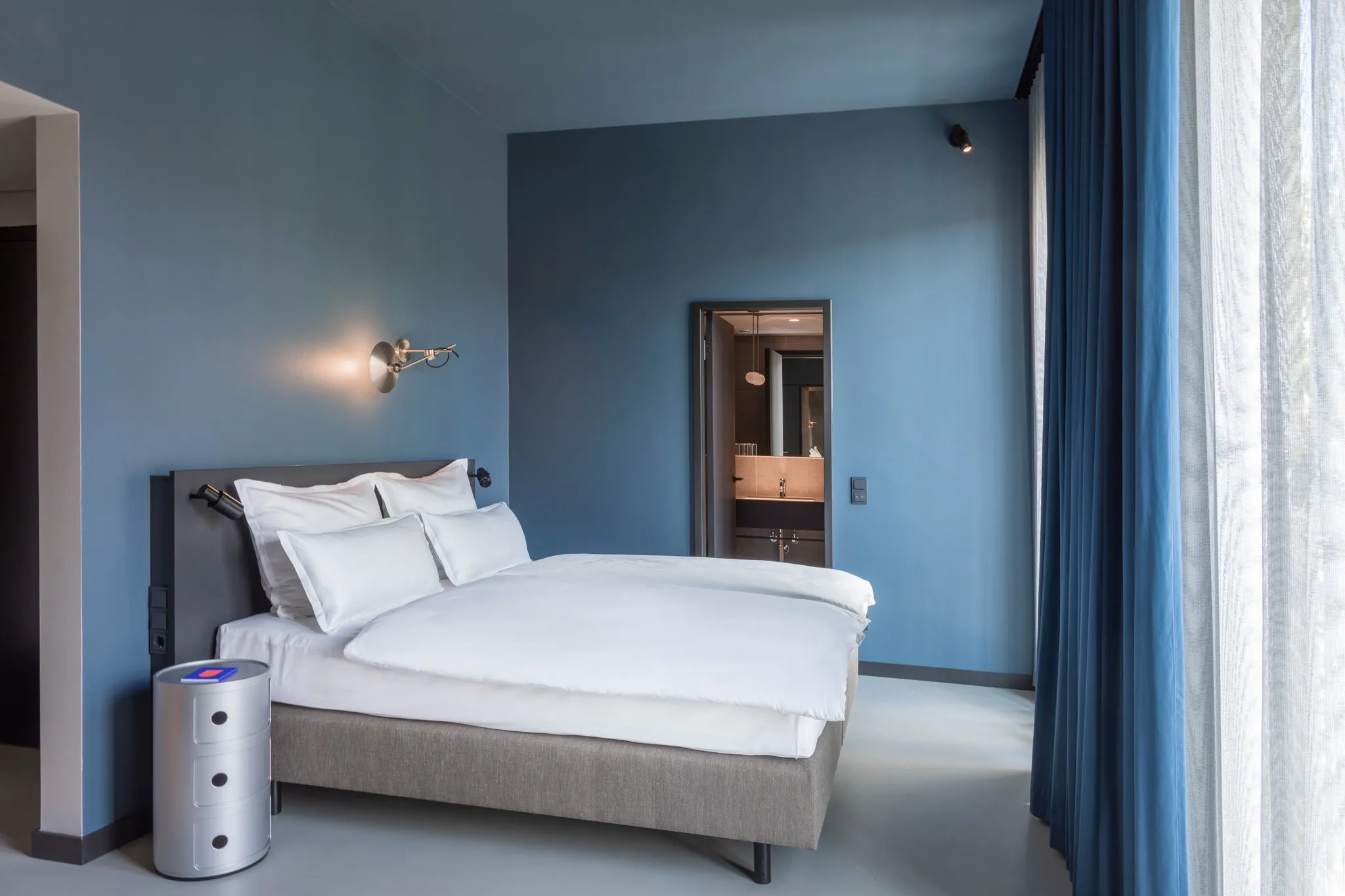 Doppelzimmer im EmiLu Hotel mit blau gestrichenen Wänden, großem Bett und angrenzendem Badezimmer.