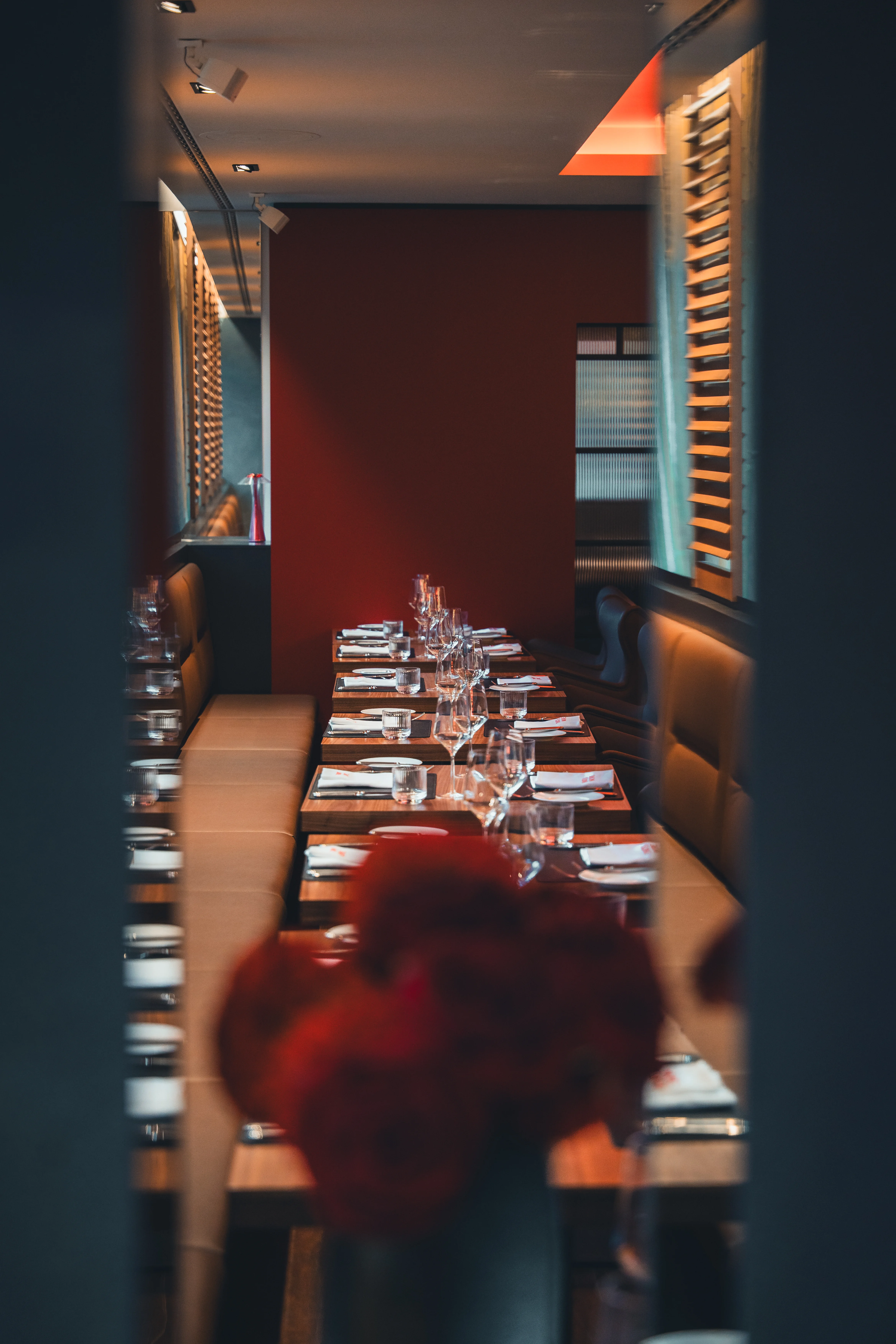 Elegant gedeckter langer Tisch in einem stilvollen Restaurant mit roten Wänden, Gläsern und Besteck, bereit für eine Feier oder ein Dinner.