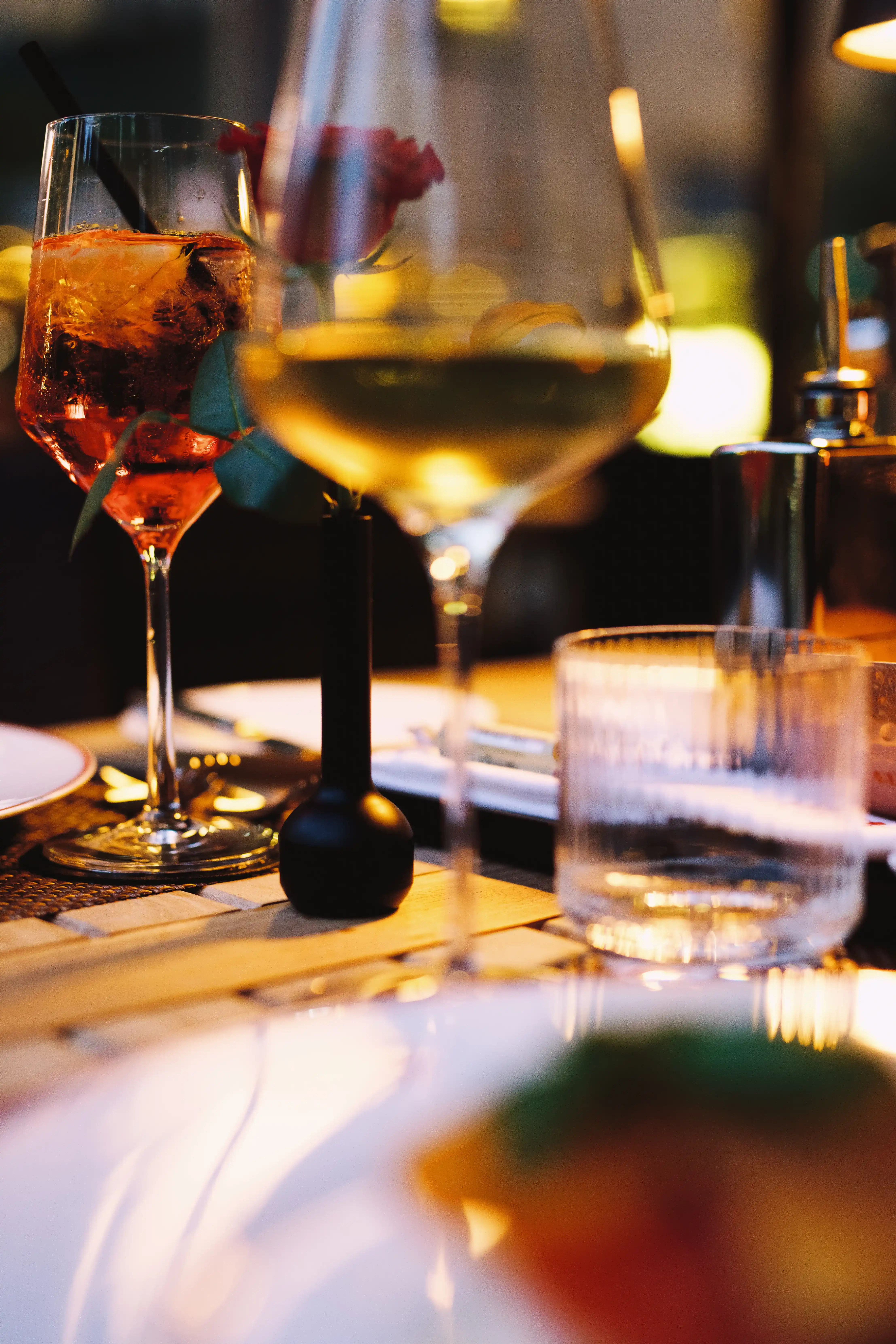 Stimmungsvolle Nahaufnahme von Aperol Spritz und Weißwein auf einem gedeckten Terrassentisch bei Abendlicht.