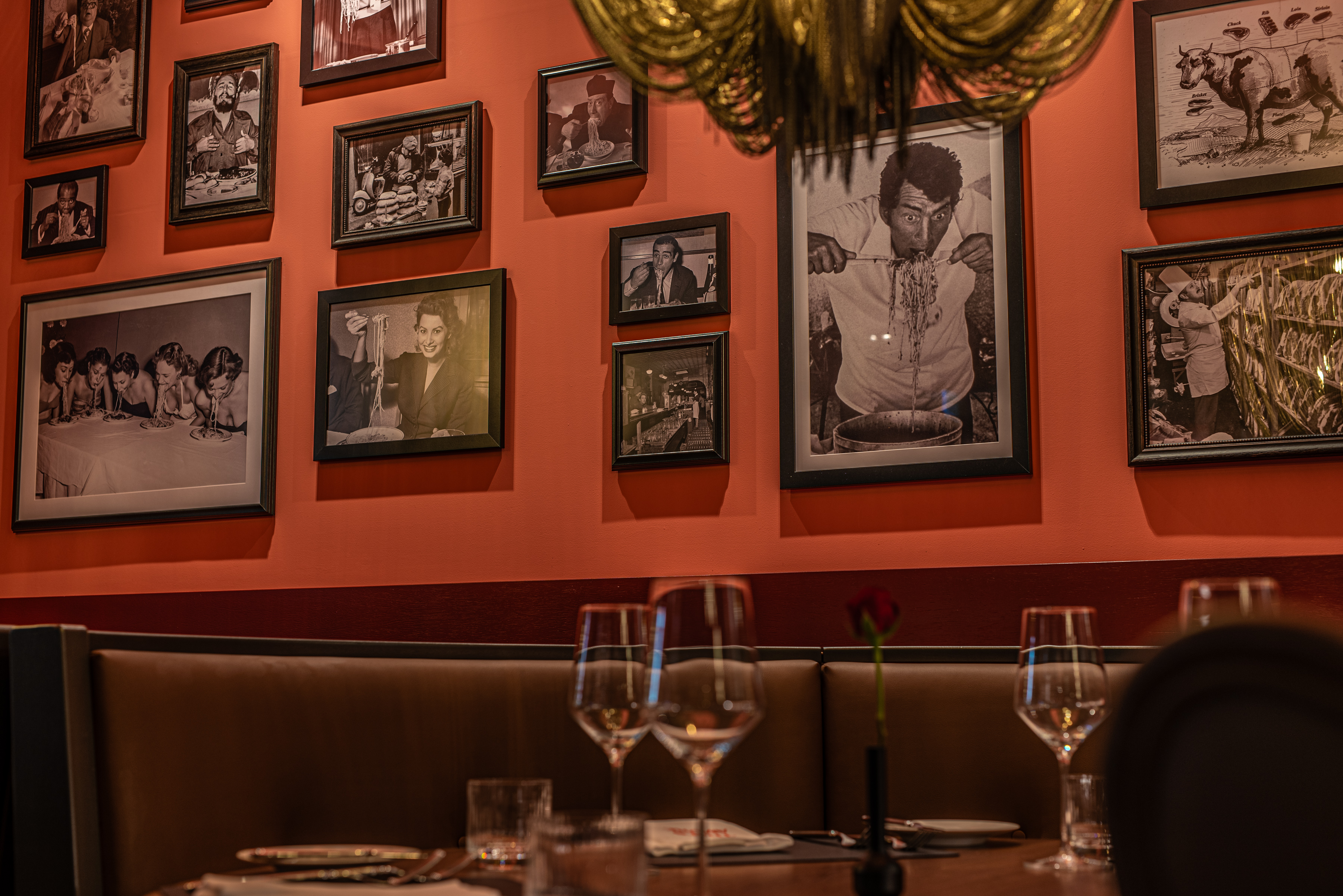 Wand mit gerahmten Schwarz-Weiß-Fotografien in einem Restaurant, davor ein gedeckter Tisch mit Gläsern und einer roten Rose.