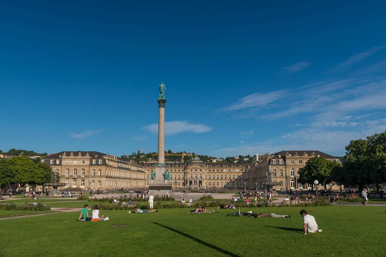 Menschen entspannen sich auf dem Rasen des Schlossplatzes in Stuttgart bei sonnigem Wetter, im Hintergrund das Neue Schloss und die Jubiläumssäule.