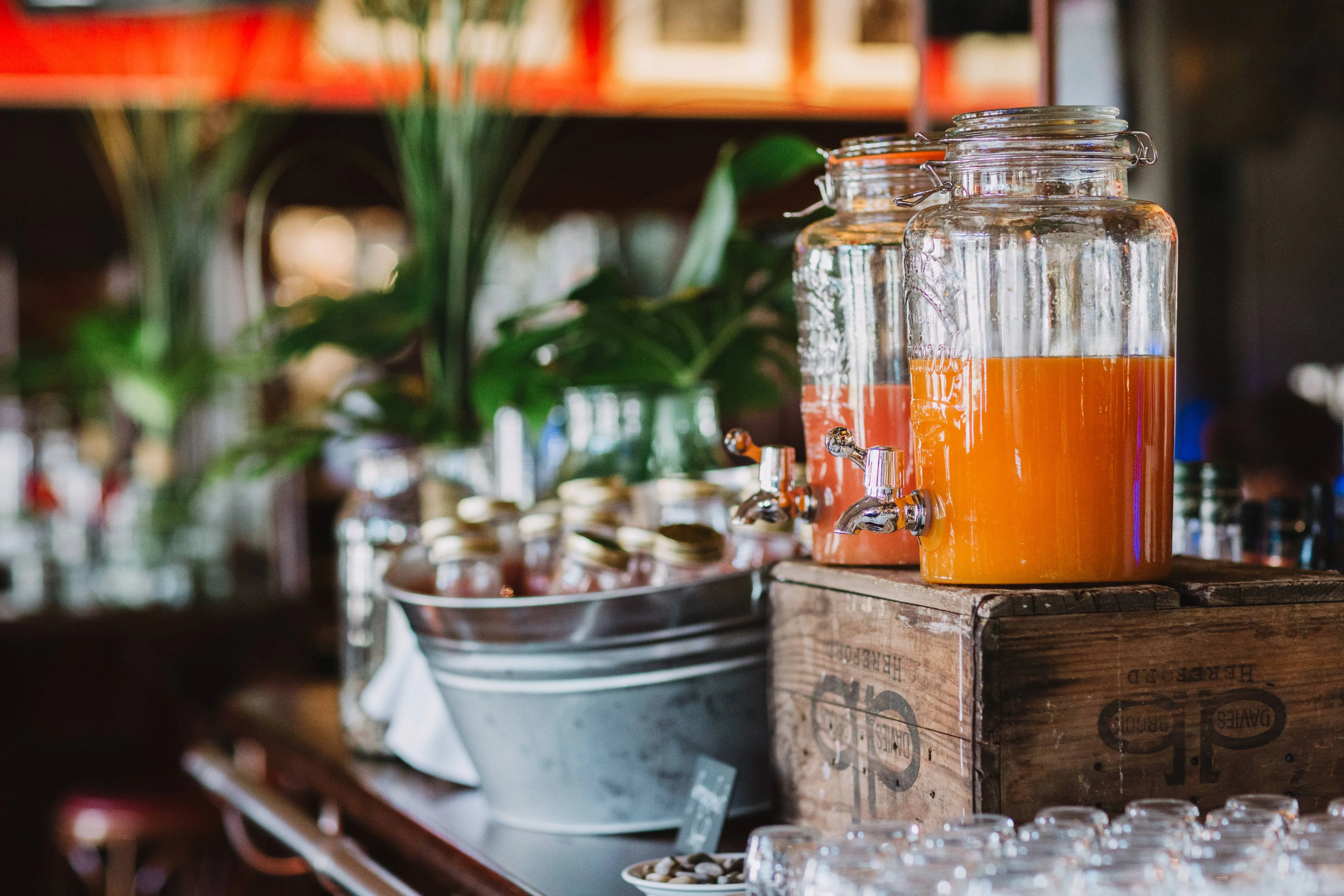 Zwei große Gläser mit frisch gepresstem Saft auf einer Holzbox, daneben weitere Flaschen und Gläser.