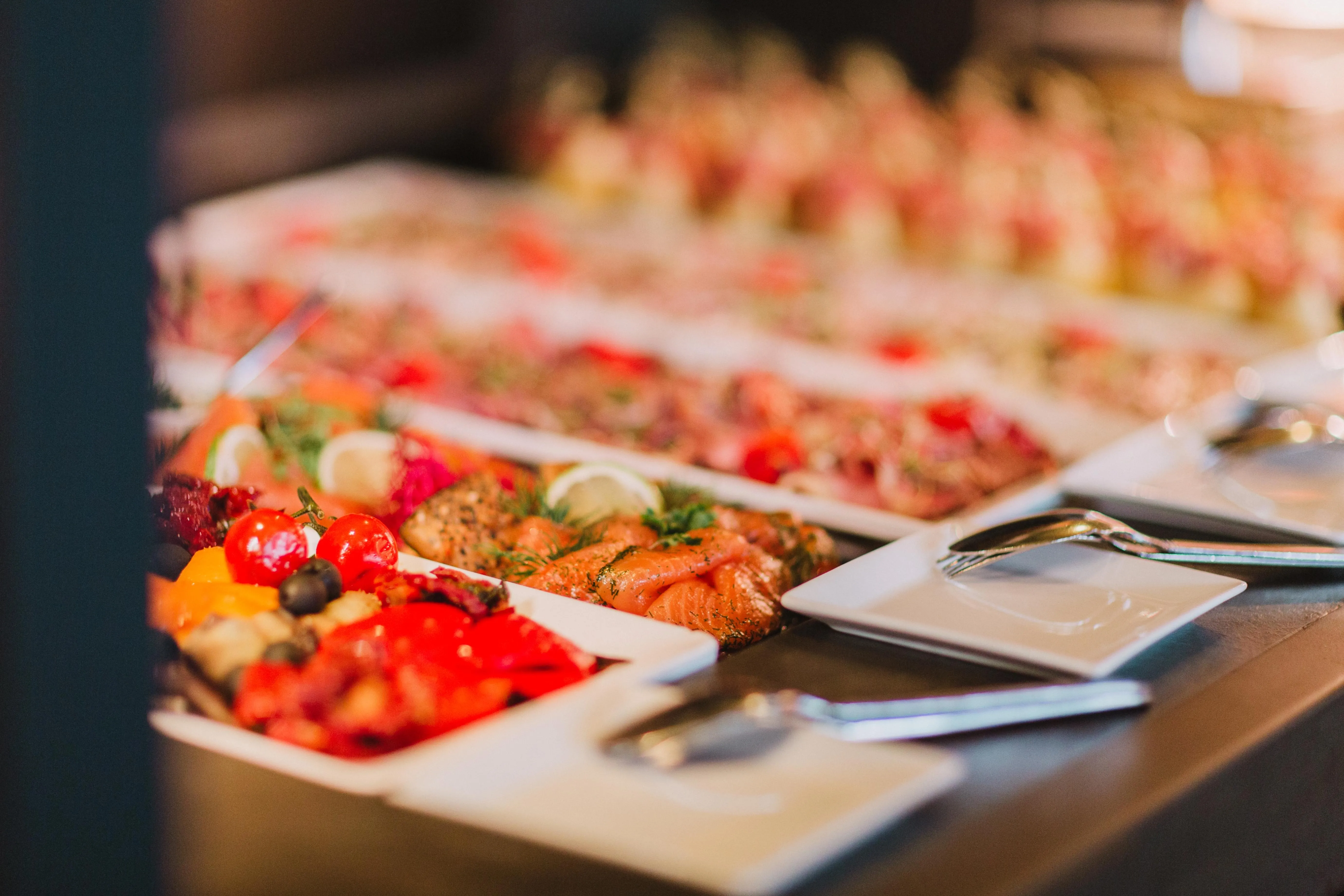 Ein Buffet mit bunten Antipasti und kalten Speisen – Tomaten, Lachs, Paprika und weitere feine Häppchen appetitlich angerichtet auf weißen Platten.