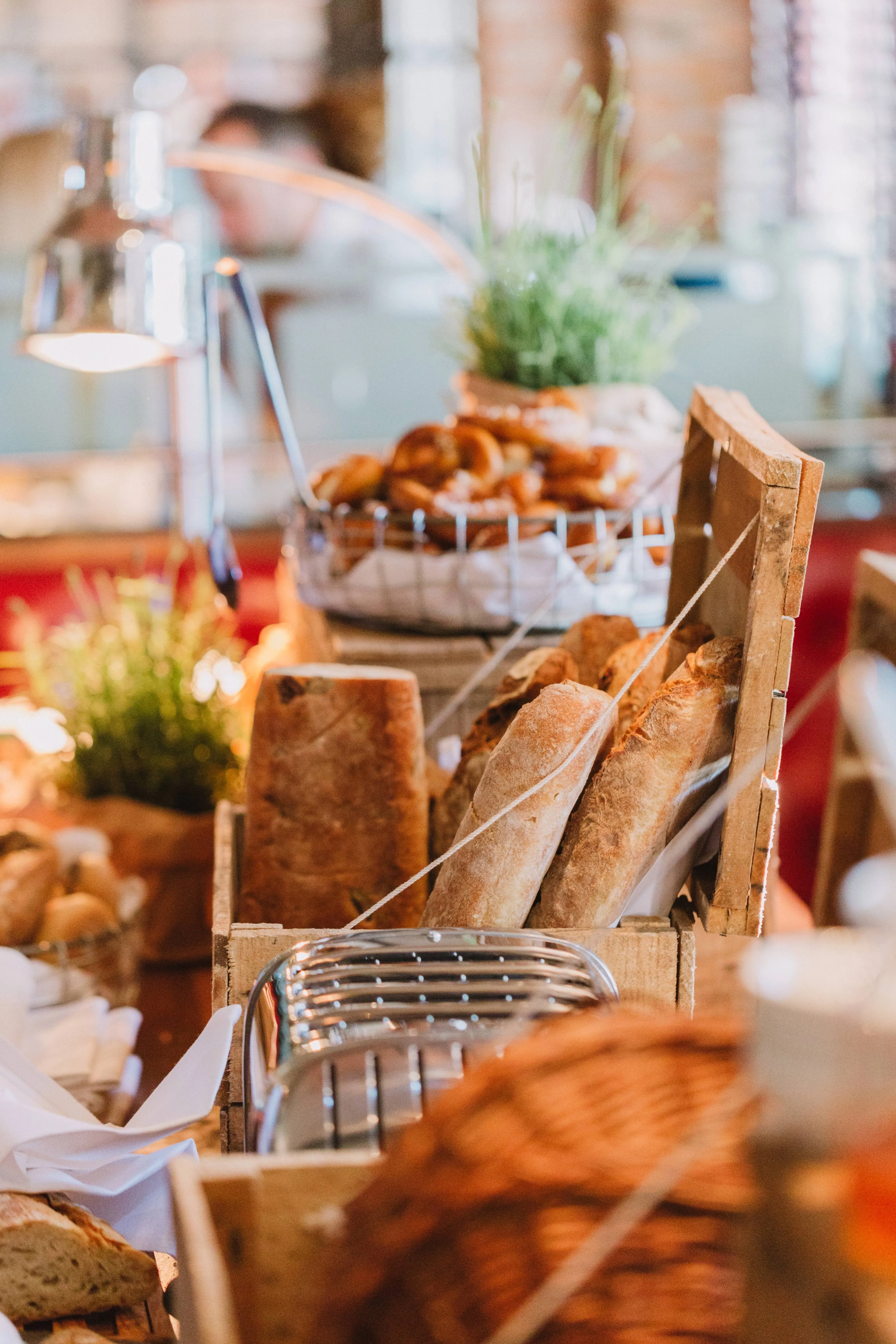 Frische Baguettes und Brötchen in rustikalen Holzkisten auf einem Buffe. Im Hintergrund einladende, warme Lichtstimmung.