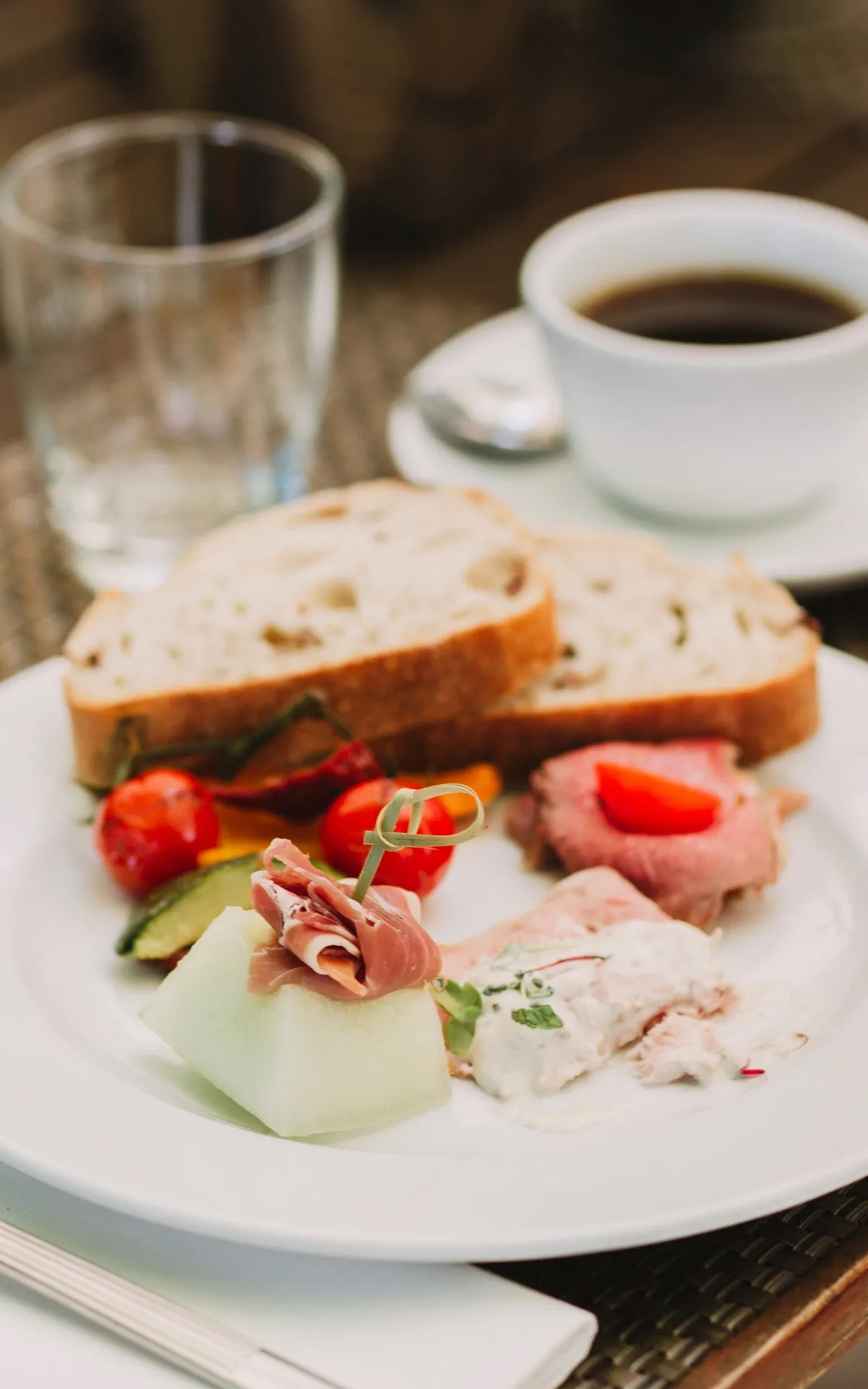 Ein gedeckter Frühstückstisch mit Brot, Aufschnitt, Melone, Saft und Kaffee – ein harmonisches Brunch-Arrangement auf geflochtener Tischunterlage.