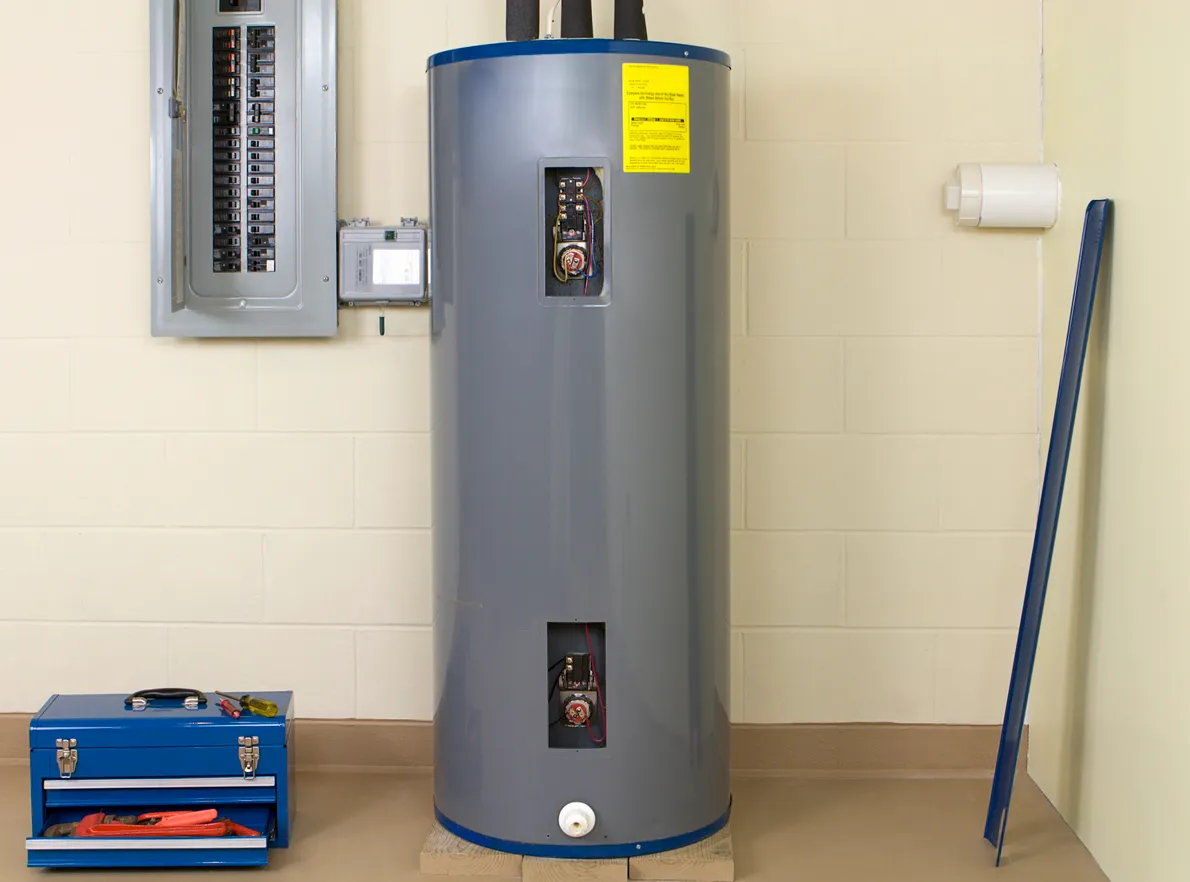 Tall water heater installed next to an electrical panel. A toolbox is on the floor next to the water heater.