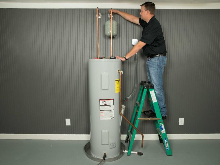 Man standing on a green ladder checks a wall valve of a water heater.