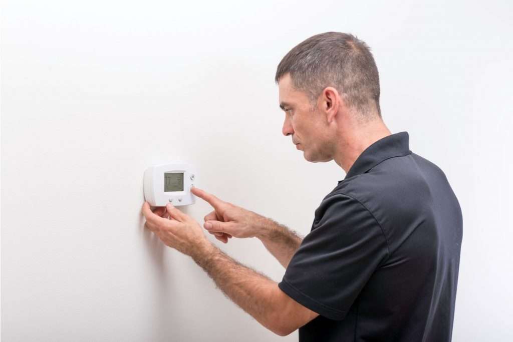 Man checks thermostat on a white wall.