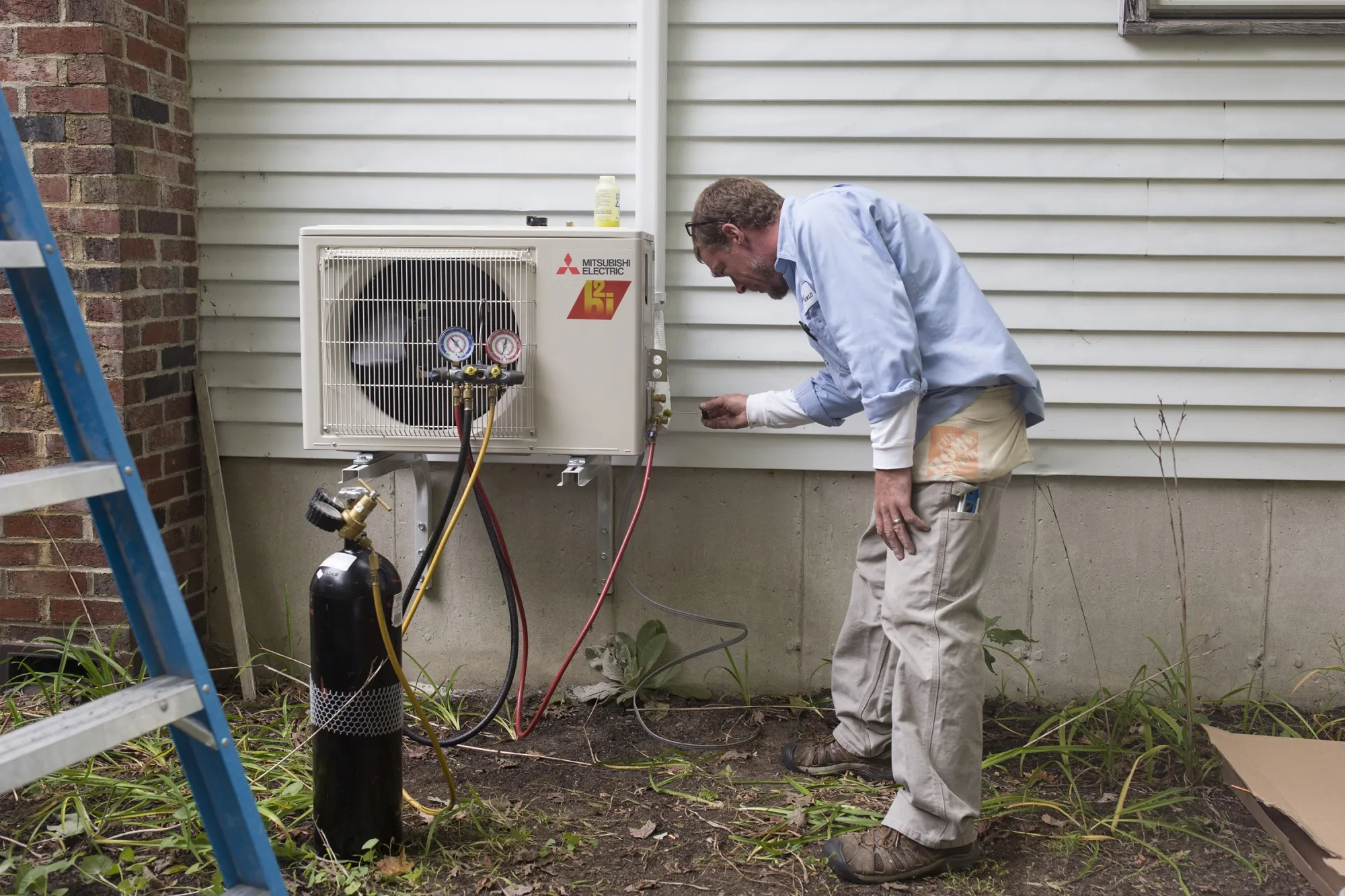 Technician checks a wall mounted heat pump unit outdoors.