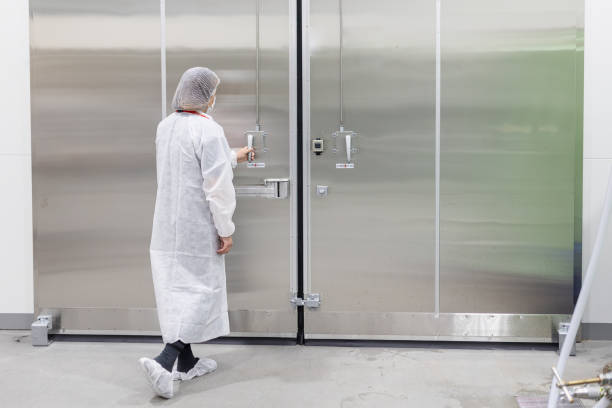 Image of a worker in a white coat and hairnet reaching for a commercial refrigeration door.