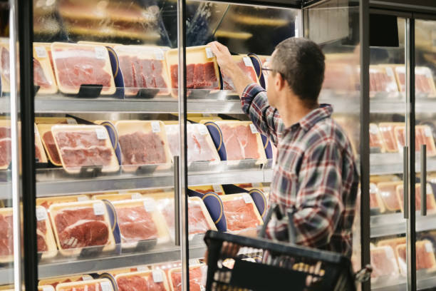 A man in plaid shirt, reaching for a package of meat in a supermarket refrigerator.
