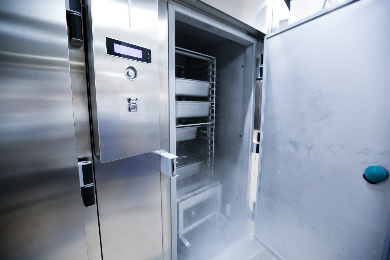 A commercial refrigerator is open, showing chafer pans inside.