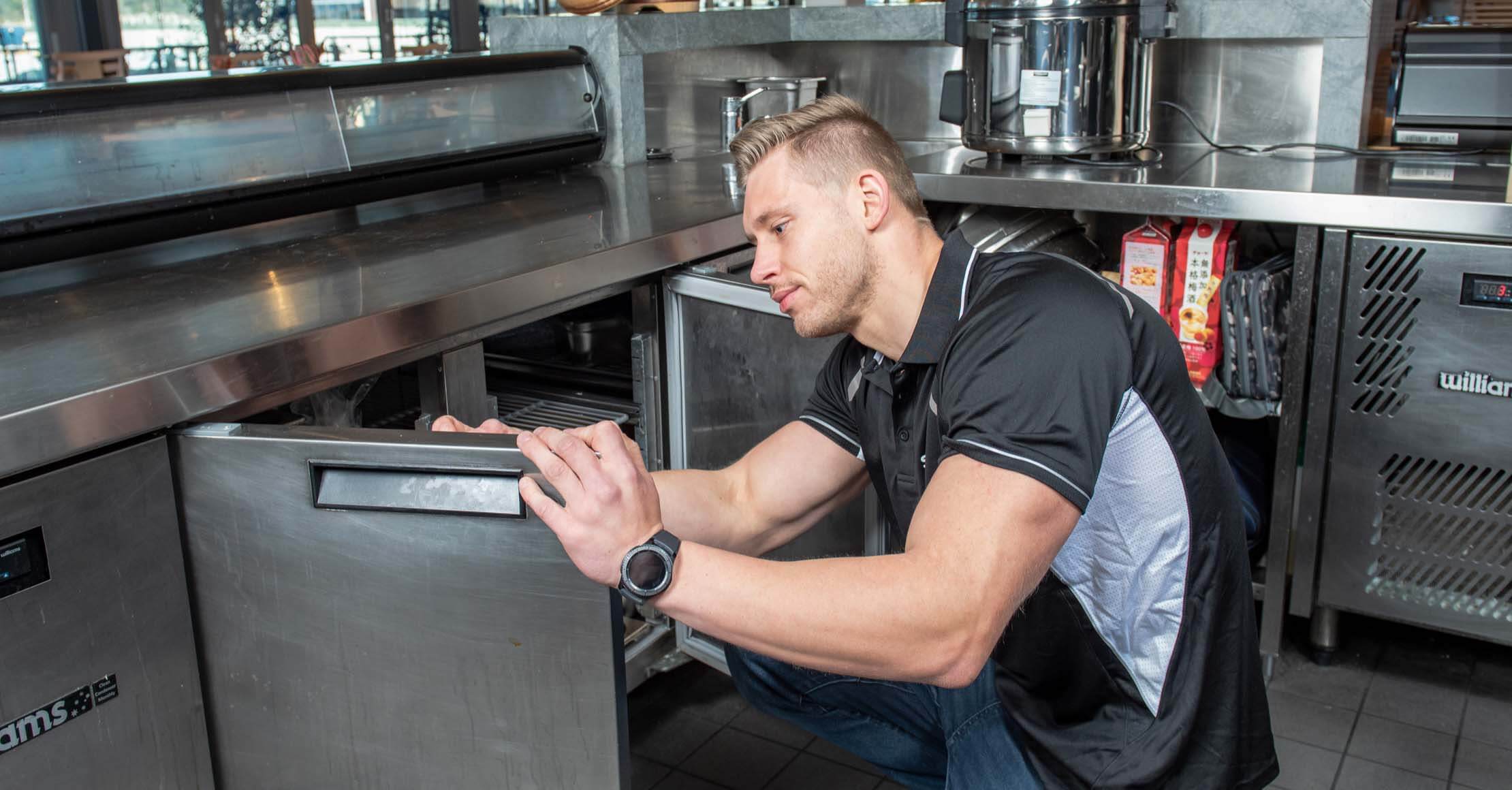 A technician checks a commercial front of house counter refrigeration, in a kitchen setting.