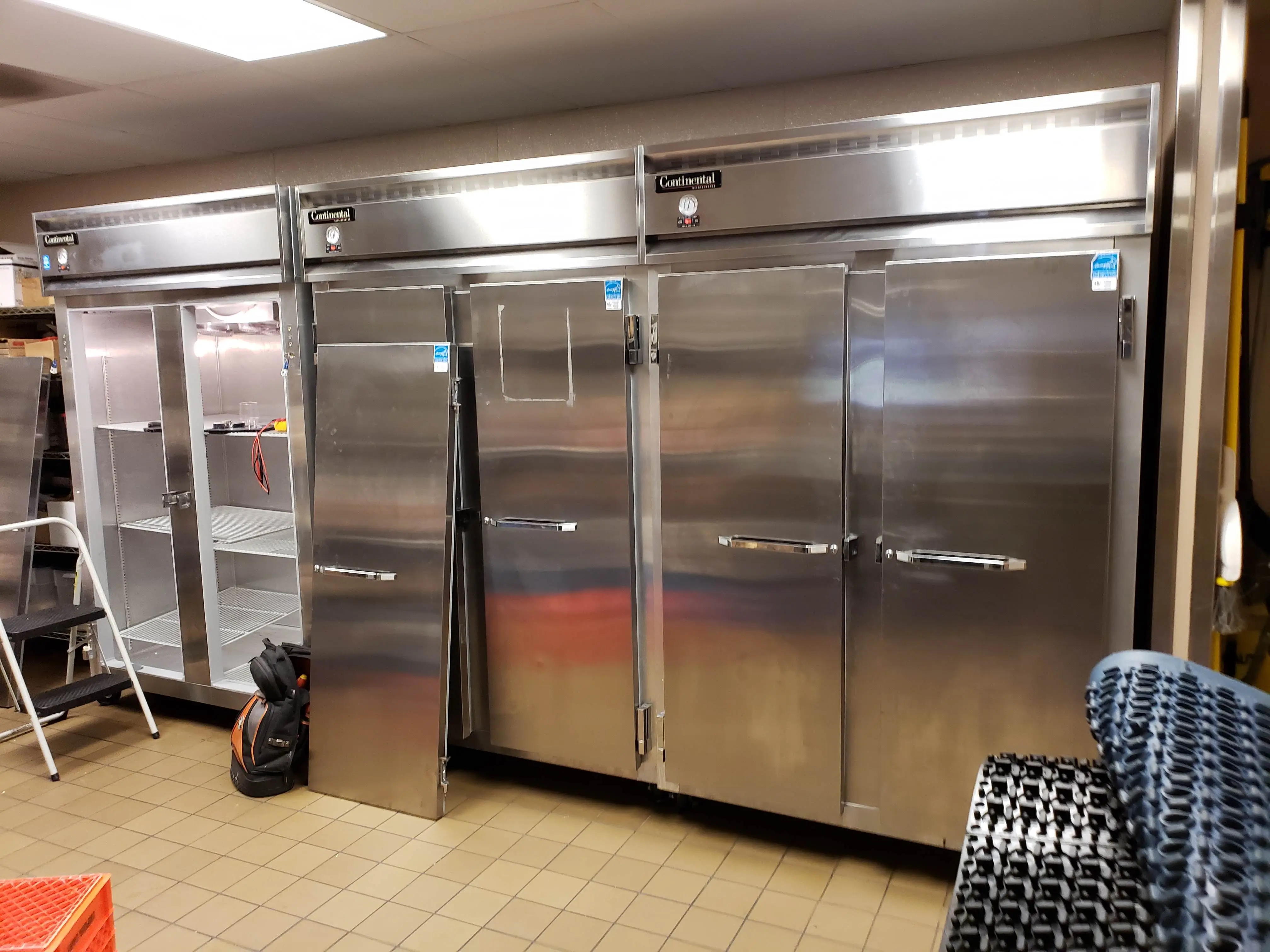 A set of commercial refrigerators. The far left refrigerator has its 2 doors off the unit.