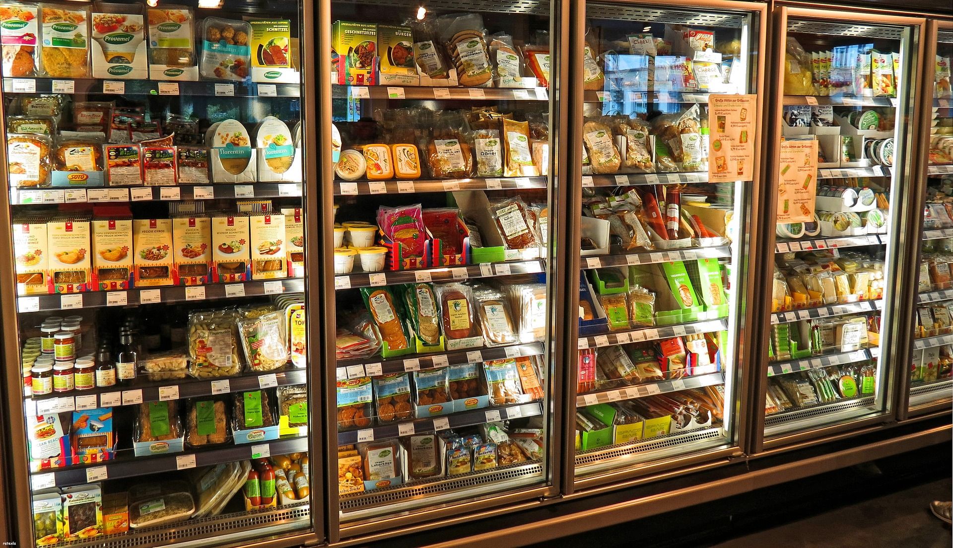 A set of commercial refrigerators, stocked with grocery products.