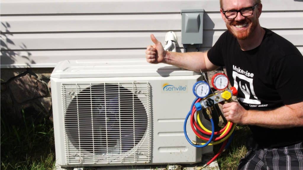 The image shows a man with a mini-split air conditioner unit. He is looking at the camera and giving a thumbs up.