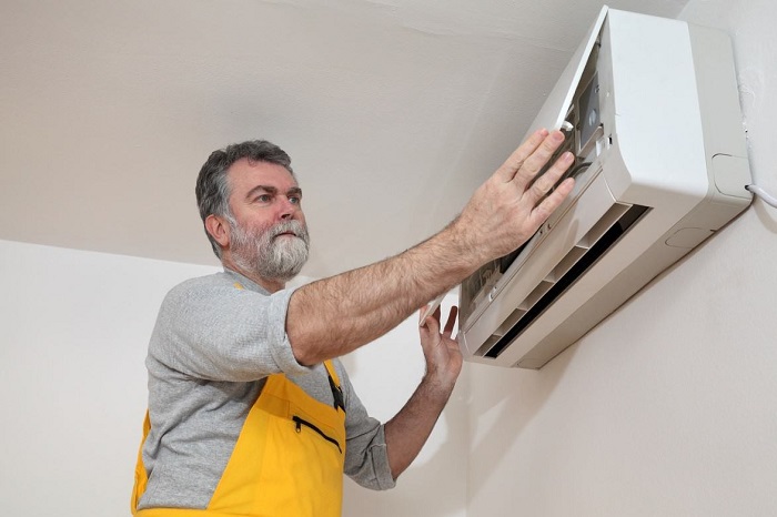 The image shows a man inspecting or working on a ductless mini-split air conditioner unit.