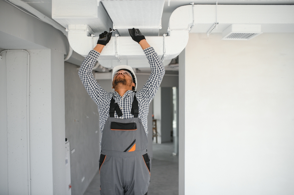 The image shows a technician working on an air duct system, likely performing air duct cleaning or maintenance.