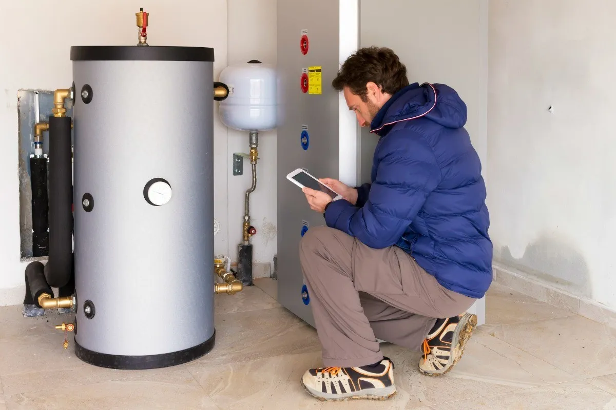 Image depicts technician checking ipad, next to a water heater.
