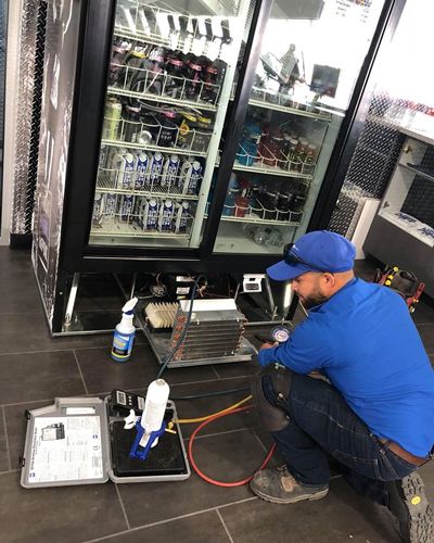 The image shows a technician servicing a commercial display refrigerator.