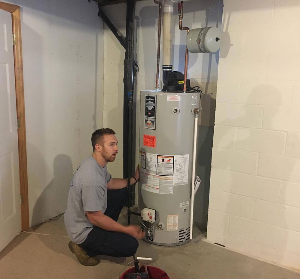 The image shows a technician examining a storage tank water heater.