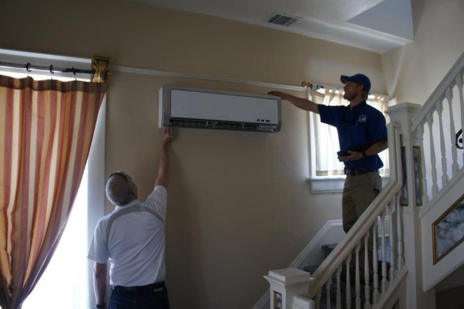 La imagen muestra a dos personas trabajando en la instalación o servicio de una unidad de aire acondicionado mini-split sin ductos.