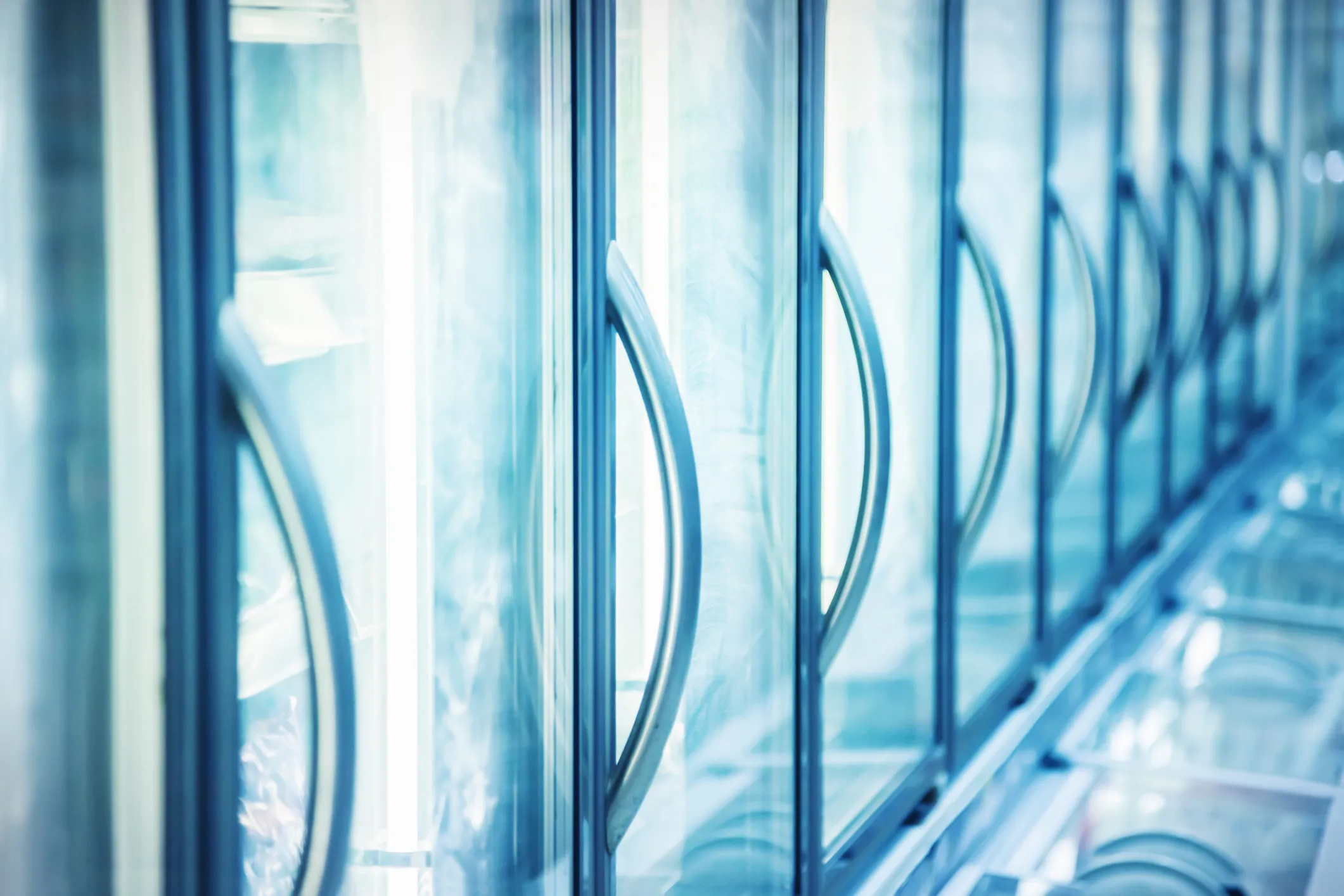 A close-up, angled view of a row of commercial glass refrigerator doors with handles, commonly found in grocery stores.