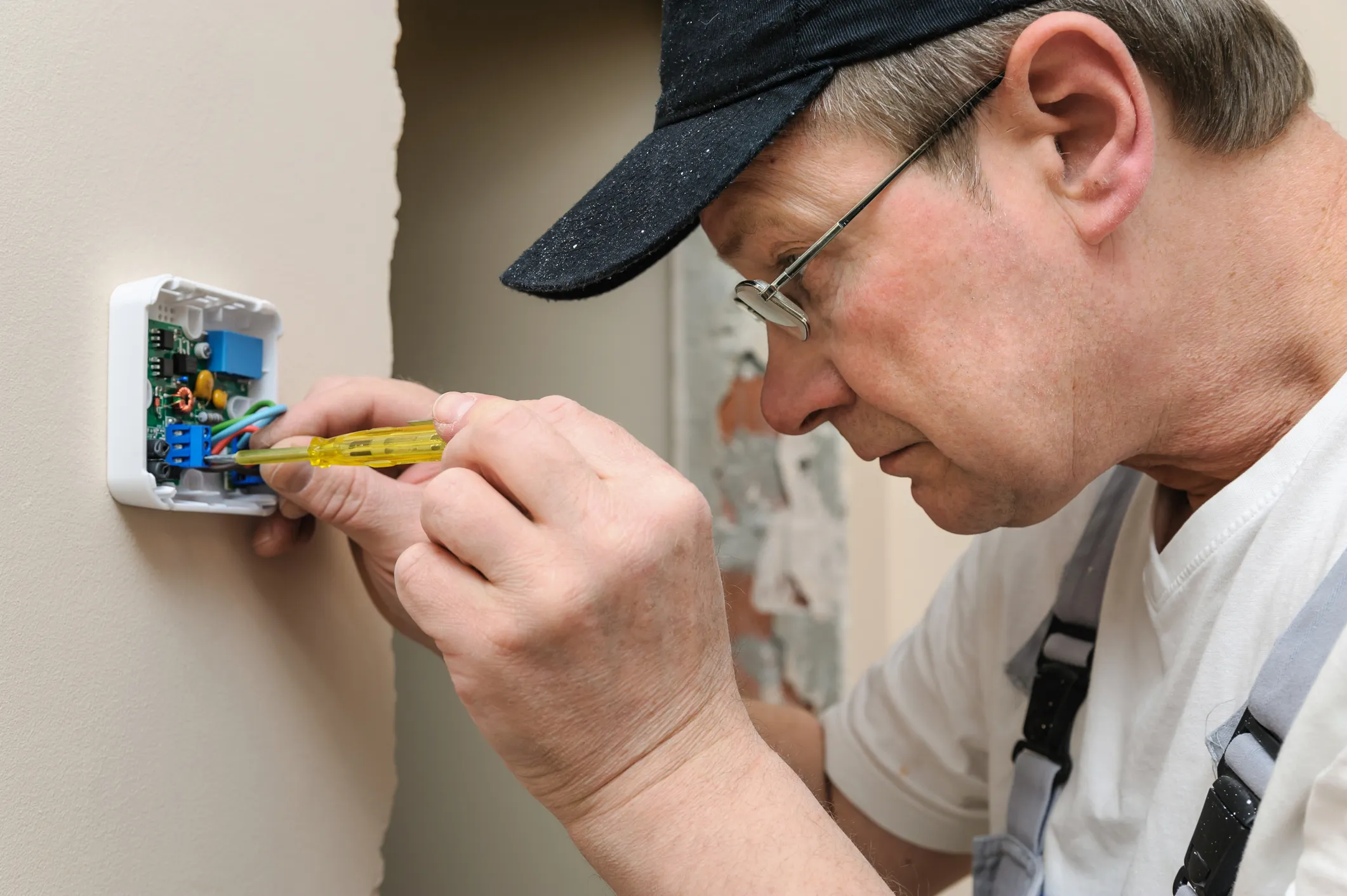 HVAC technician using a screwdriver to connect wiring to the circuit board during a thermostat replacement.