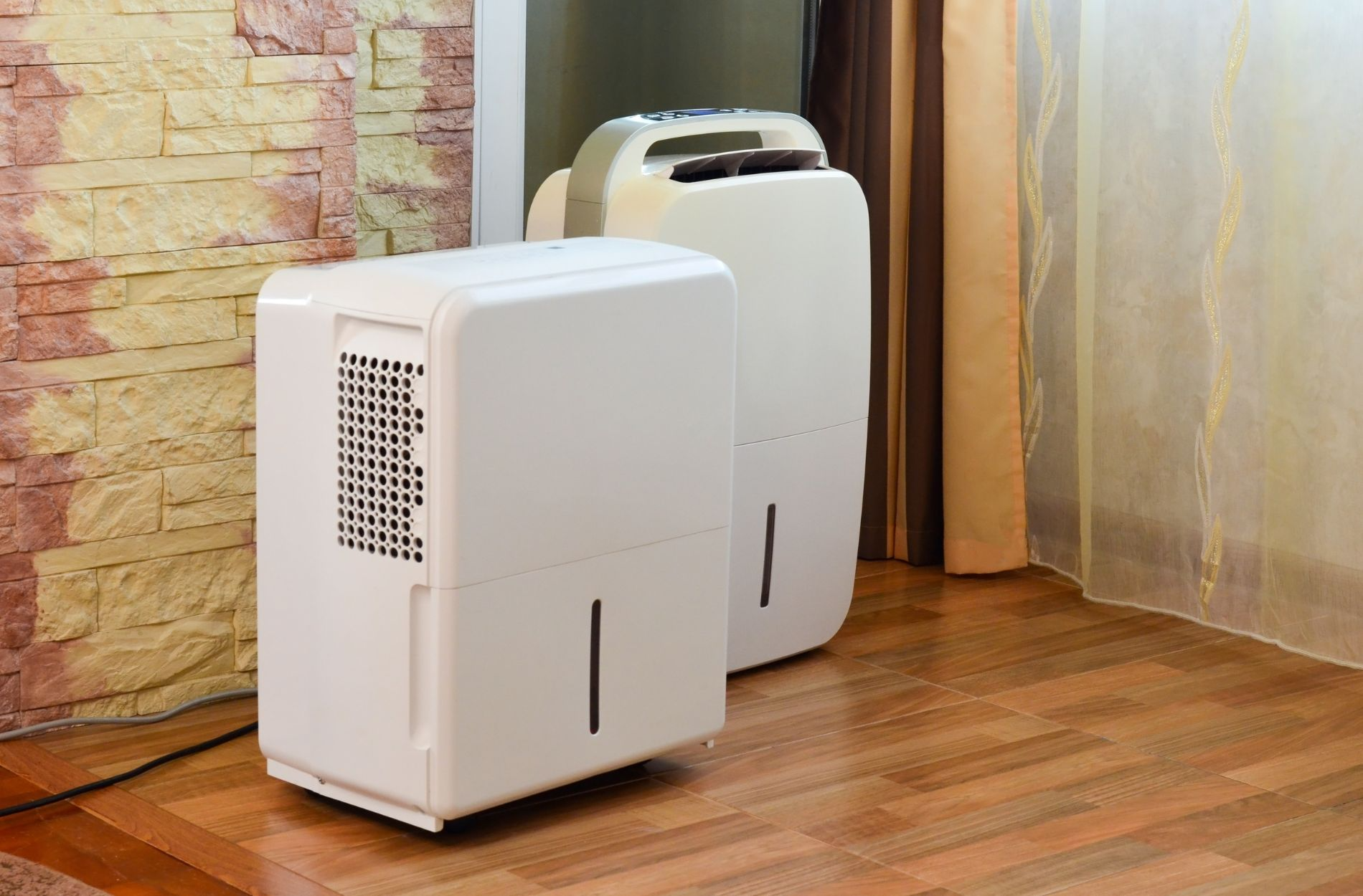 Two white home dehumidifiers on wooden floor.