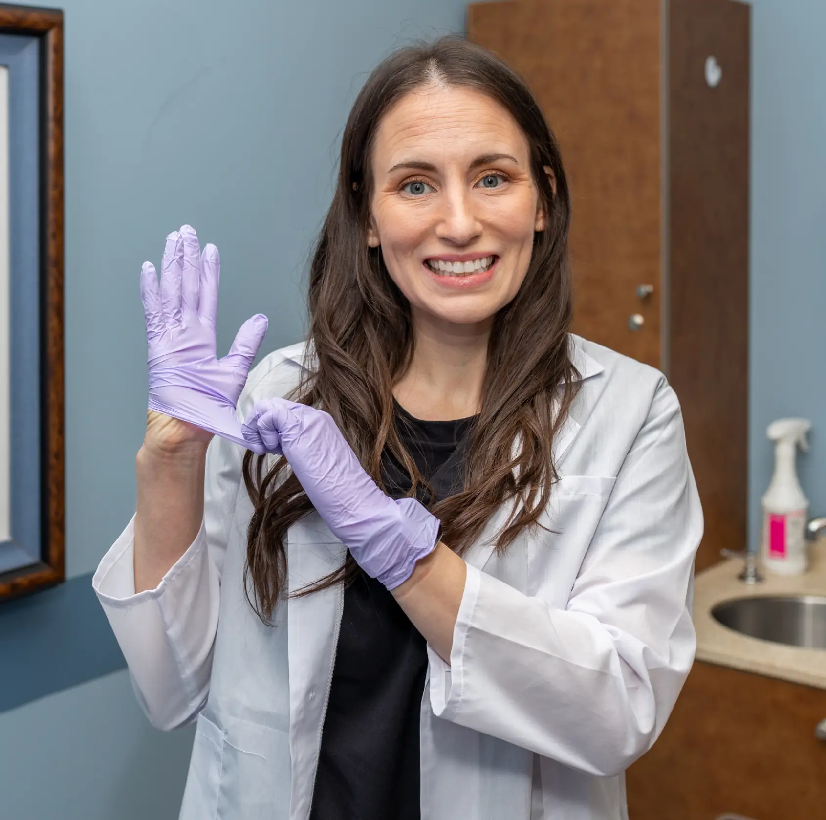 Two women in lab coats sit together, smiling and forming a heart shape with their hands.