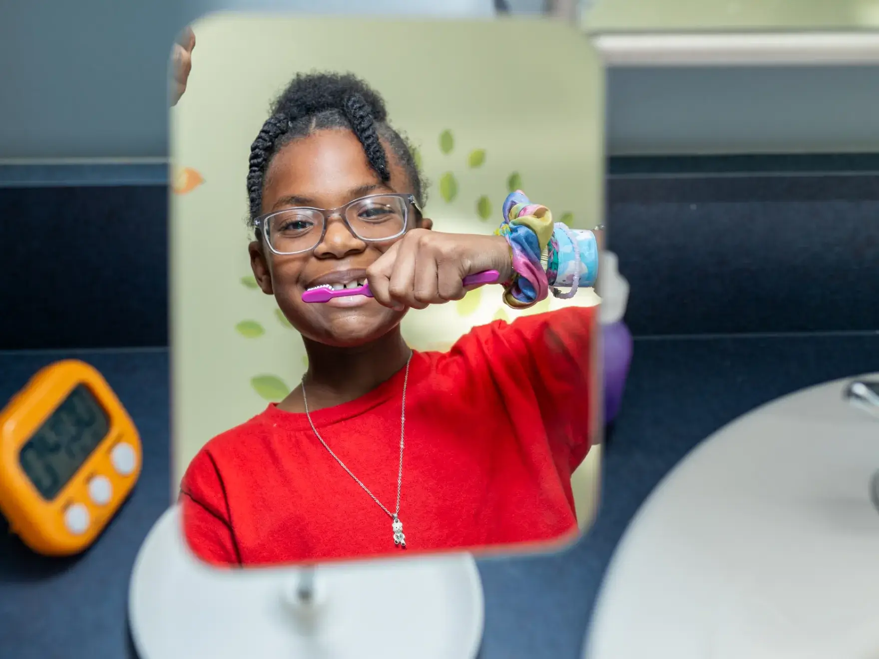 A young girl brushing her teeth in front of a mirror.