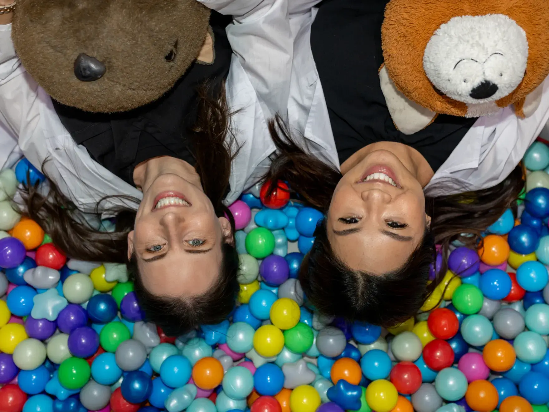 Dr. Fillmore and Dr. Siripon laying in a ball pit with teddy bears.
