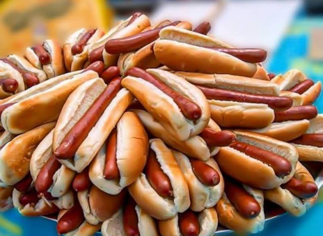 Pile of hot dogs with buns stacked on a blue surface with blurred background.