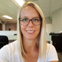 Smiling woman with long blonde hair and glasses in an office setting.