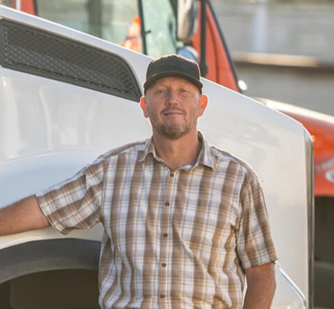 Man in a plaid shirt and black cap standing next to a white truck.