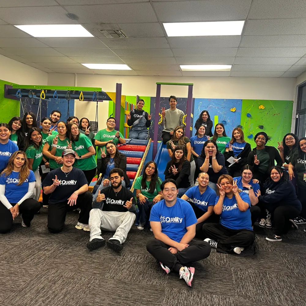 Large group of Alongside ABA staff in a sensory gym, smiling and posing together.