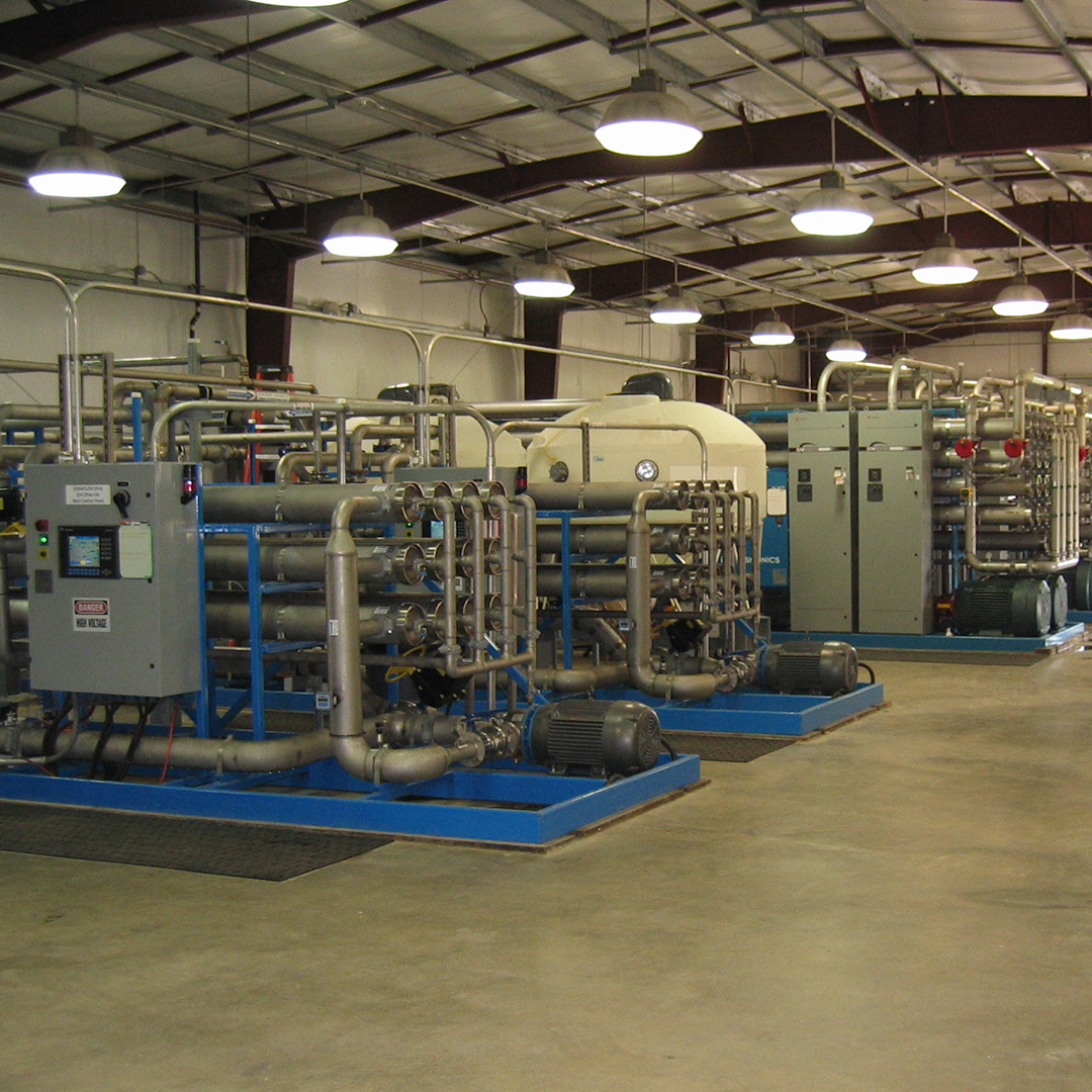 Industrial filtration equipment with metal pipes, pumps, and control panels inside a large factory building.