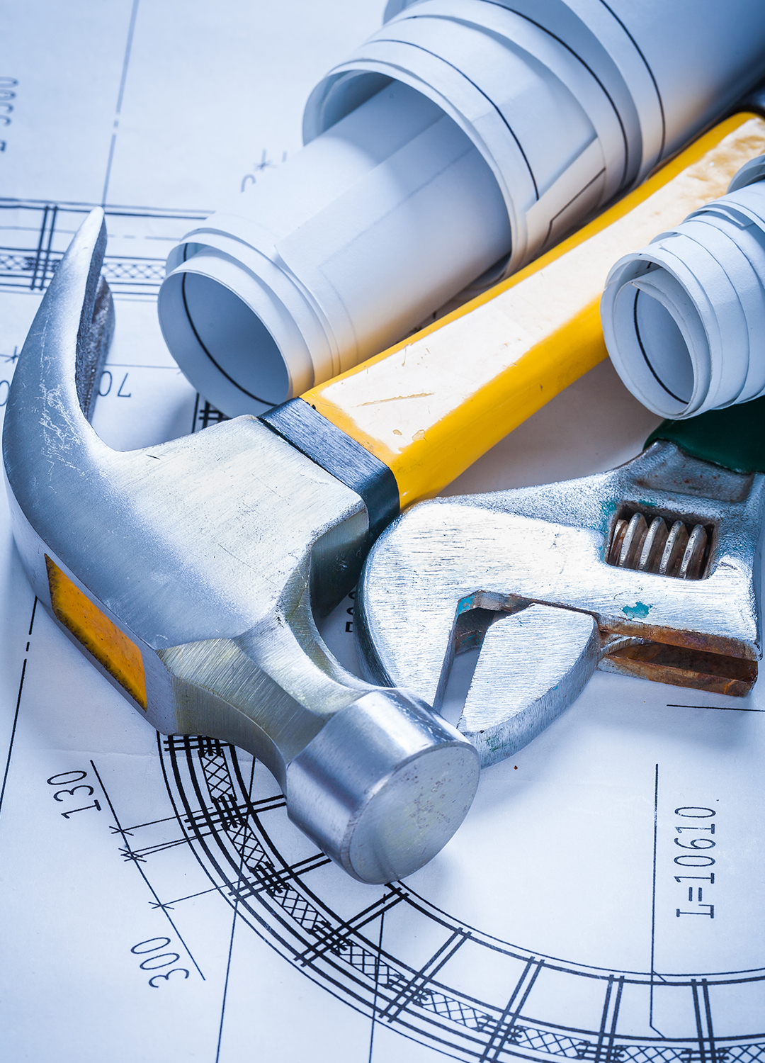 Hammer and adjustable wrench placed on rolled-up blueprints with architectural drawings.