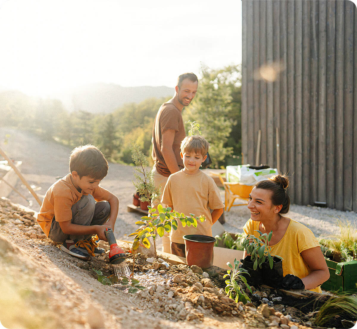 A mother and father planting plants into a garden next to their home with their two young sons.