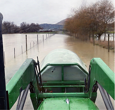 A tractor driving down a farm track that is covered in flood water.