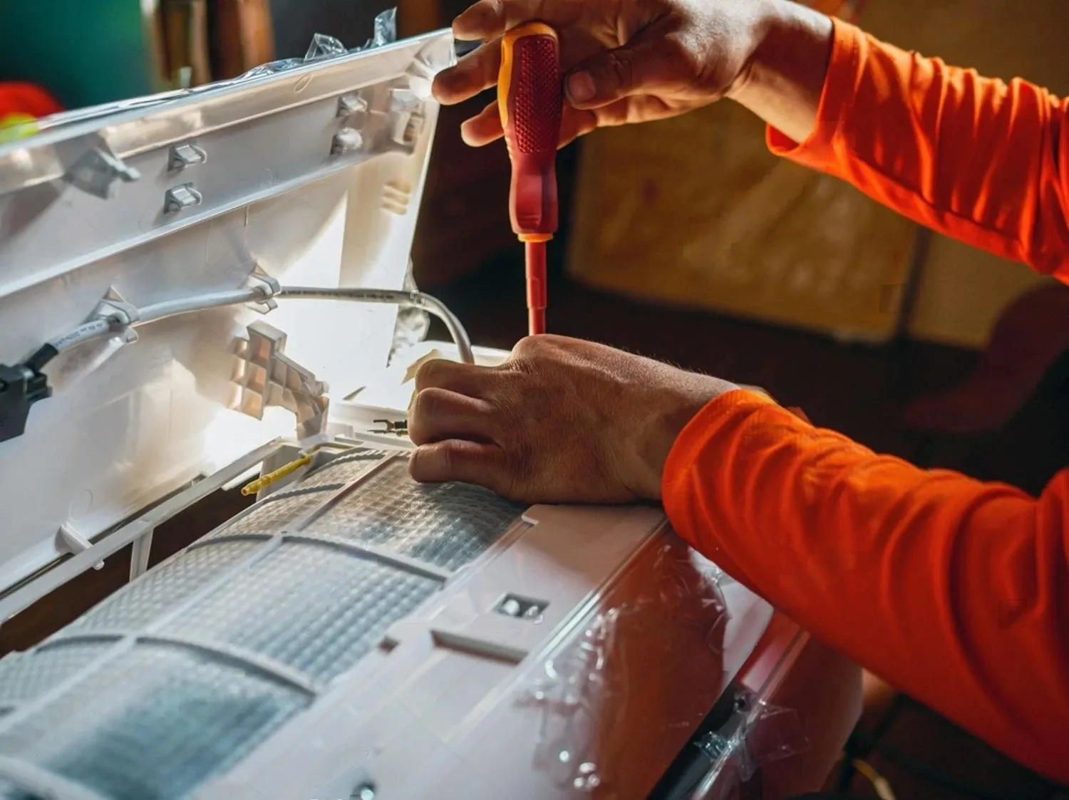 Hands in orange sleeve using red screwdriver on technical equipment