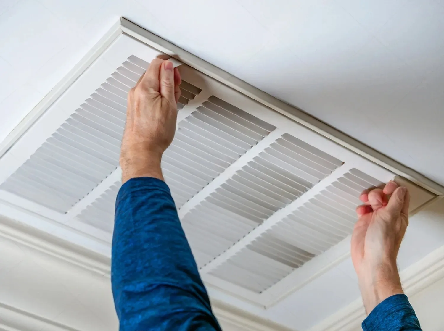 Hands opening a ceiling air vent or return air grille