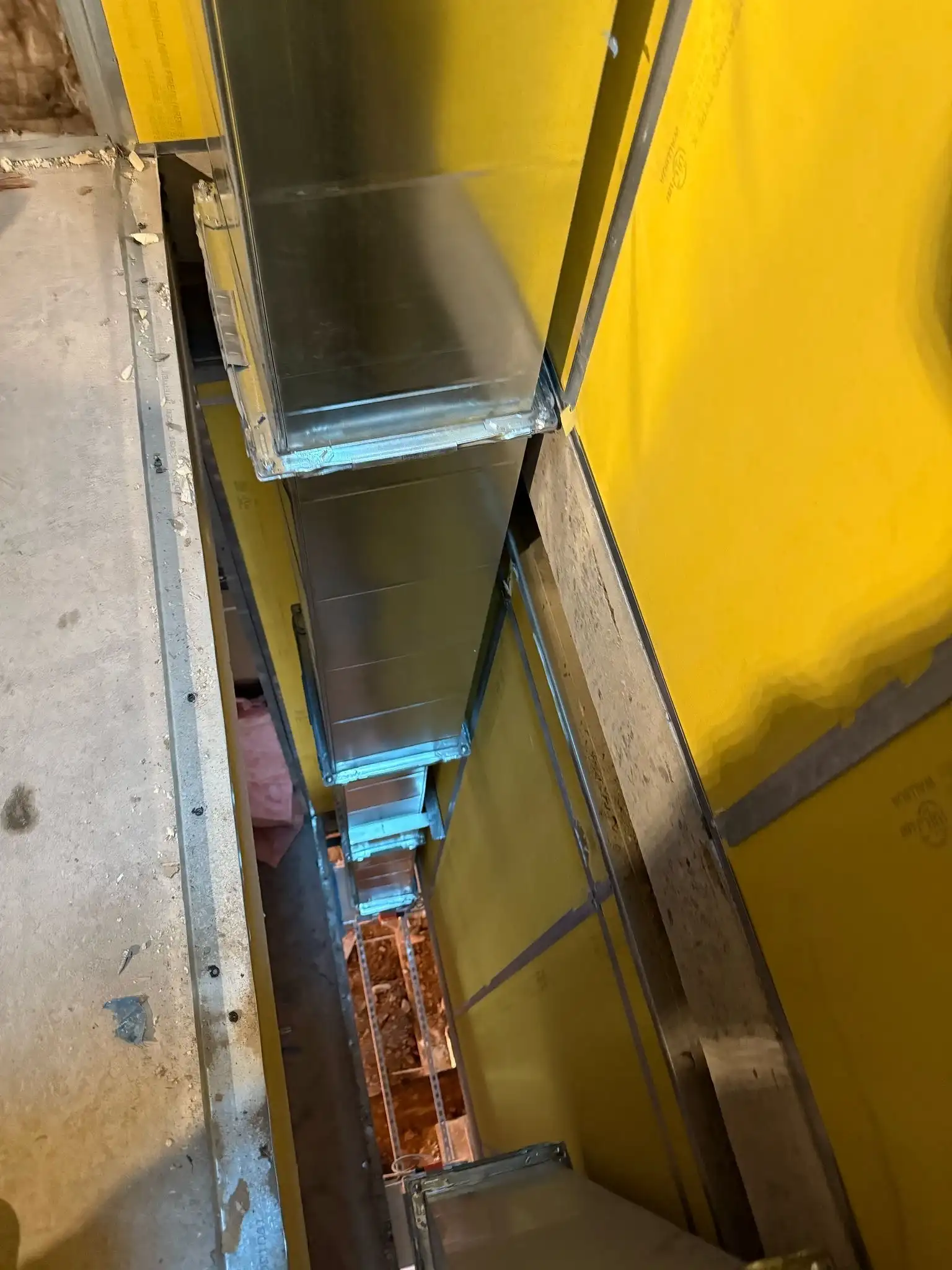 Vertical metal duct installed behind a yellow wall section