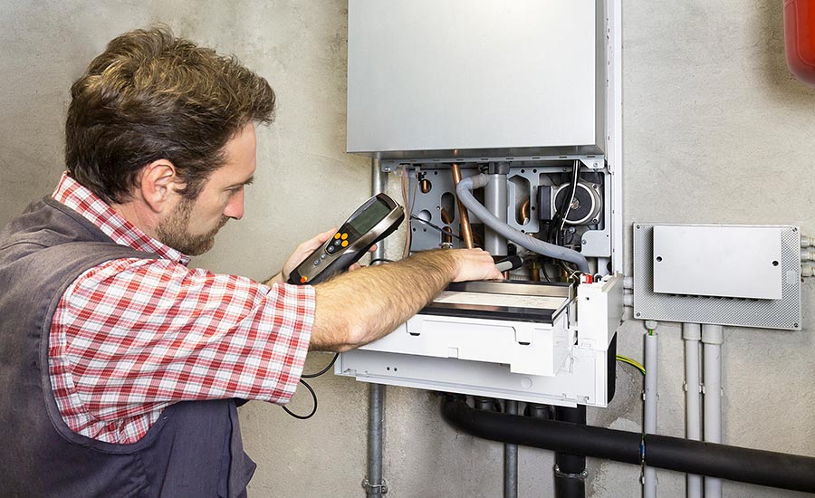 Technician in safety glasses inspecting industrial heating system with wrench